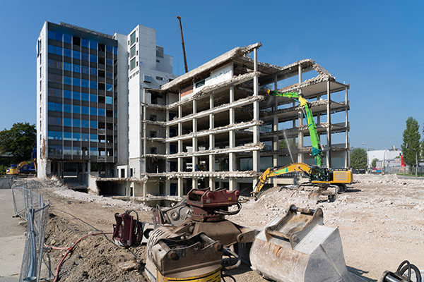 Large demolition trucks taking down an old, empty commercial builidng