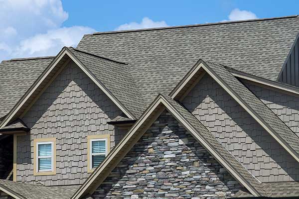 Close up of a residential roof with gray shingles on top of a large, mid-class home