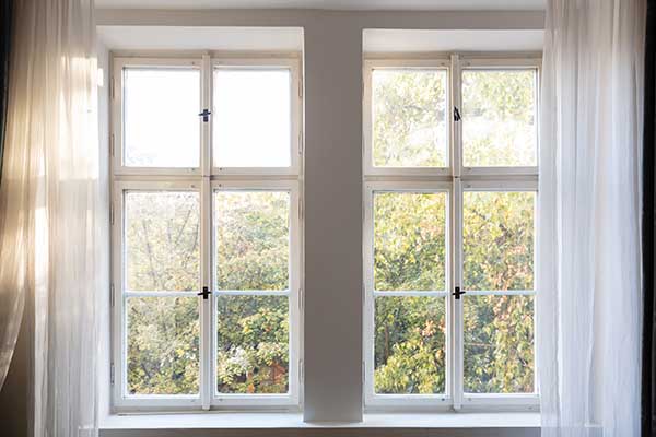 Two windows side by side inside of a home with white, transparent curtains on either side