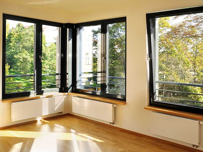 Black framed, corner windows seen from inside a home. The one on the right is being opened from the top towards the interior room