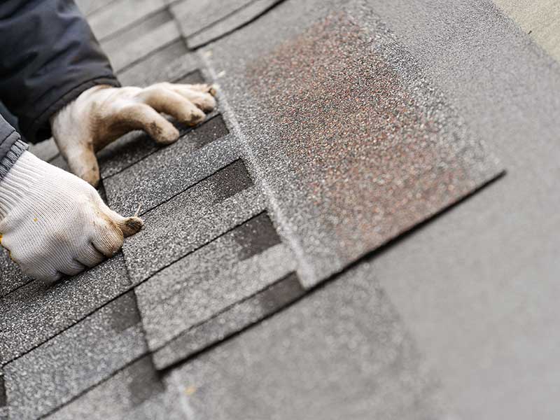 Close up of a worker's gloved hands placing down shingles on a roof